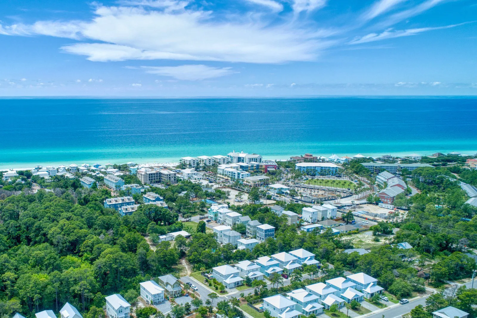 Aerial view of a 30A beach community on Florida’s Emerald Coast with rows of pastel vacation homes, resort buildings, and lush trees leading to turquoise Gulf water and white sand.