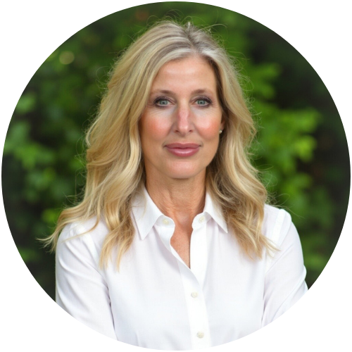 Person with long wavy blond hair wearing a white button-down shirt smiles softly at the camera, standing outdoors in front of blurred green foliage.