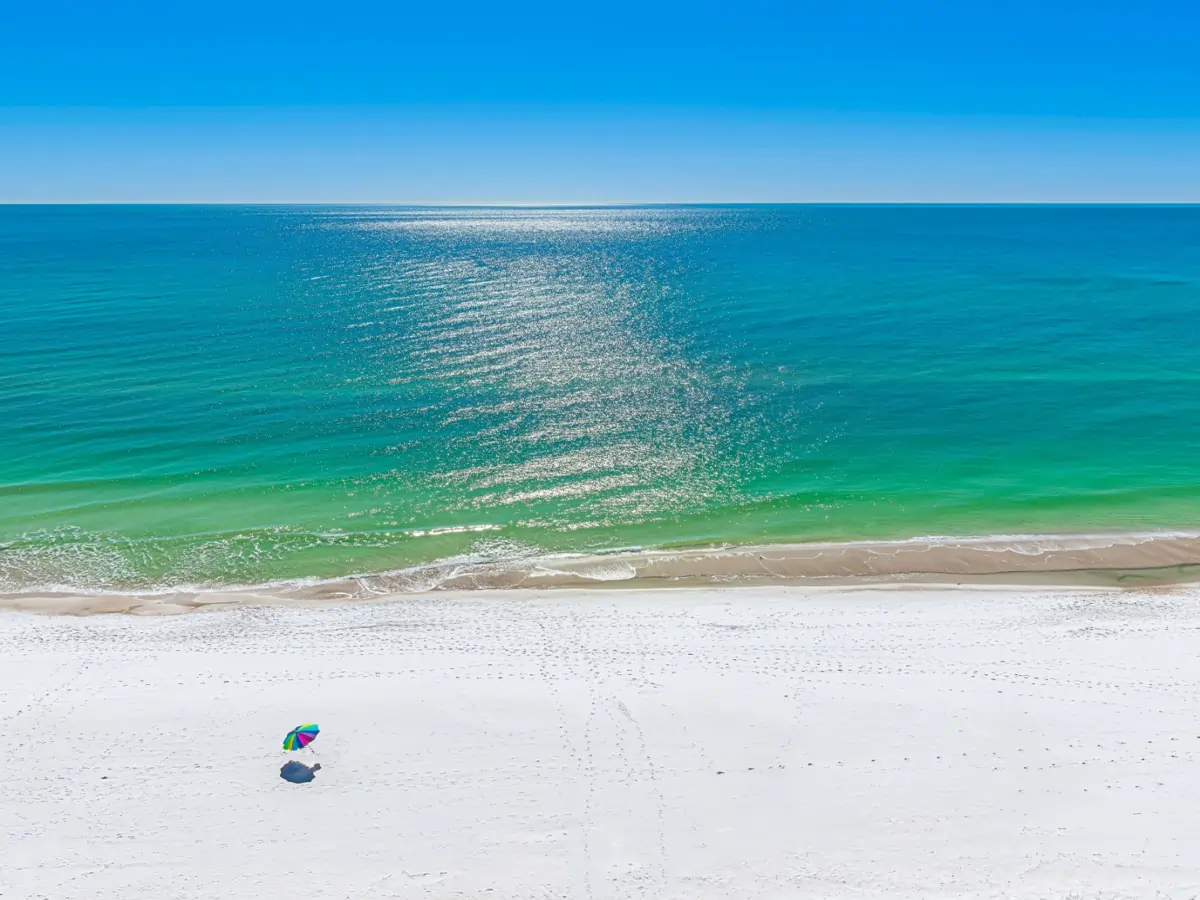 Panama City Beach shoreline with emerald-green Gulf water, sugar-white sand, and a single colorful beach umbrella on an otherwise empty stretch of coast.