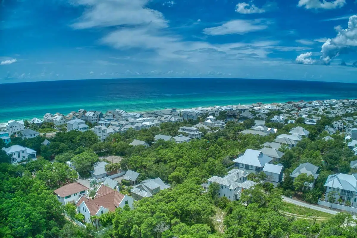 Aerial view of a 30A beach community on Florida’s Emerald Coast with rows of pastel vacation homes, resort buildings, and lush trees leading to turquoise Gulf water and white-sand shoreline.