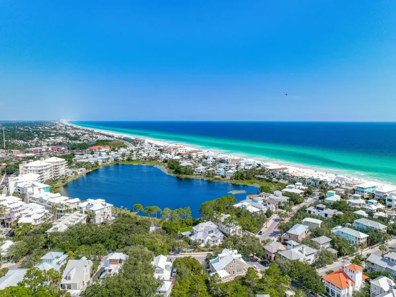 Carillon Beach aerial with a coastal dune lake, pastel vacation homes, and a long stretch of white-sand shoreline along emerald-green Gulf water on Florida’s Emerald Coast.